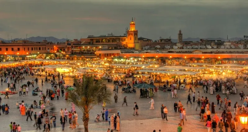 A panoramic view of Marrakesh at dusk, showcasing vibrant colors in the sky and illuminated cityscape of morocco travel tips 