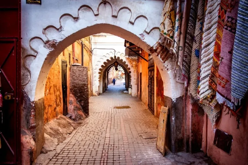  A narrow alleyway lined with aged buildings, showcasing the charm of an old city with cobblestone paths and historic architecture.While Marrakesh Tours.