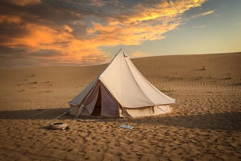 A tent stands in the desert, silhouetted against a vibrant sunset that paints the sky in warm hues While: luxury morocco desert tour 