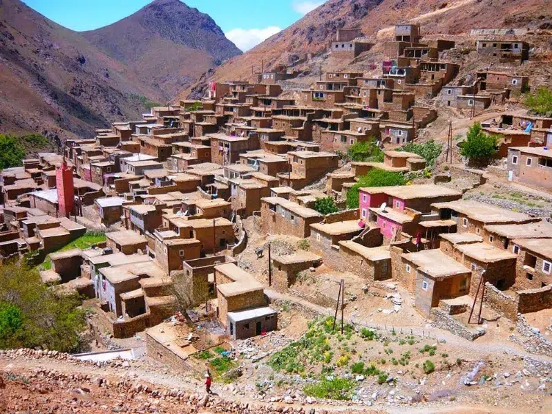 A serene mountain village showcasing a cluster of houses surrounded by majestic mountains and vibrant nature.While atlas mountains tours 