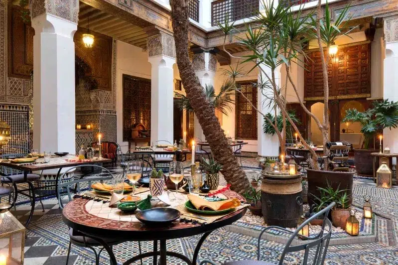 A spacious restaurant interior featuring a large table surrounded by elegant chairs, inviting for gatherings and dining.While Morocco travel Deals