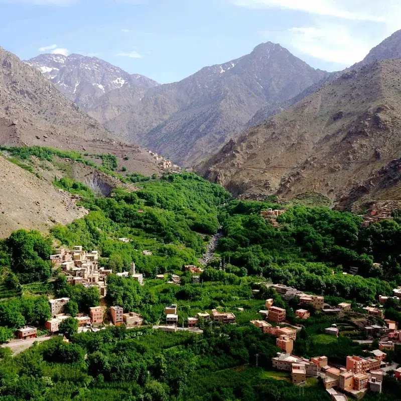 A picturesque mountain village nestled in a lush green valley, surrounded by towering peaks and vibrant nature.While atlas mountains tours