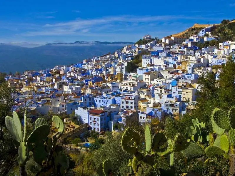 A scenic view of Chefchaouen, Morocco, showcasing its iconic blue buildings and mountainous backdrop. While visit chefchaouen