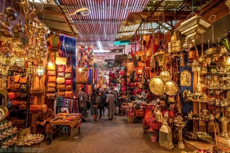 A bustling market in Marrakesh, Morocco, filled with vibrant stalls, colorful textiles, and lively shoppers exploring the scene.While Marrakech Tours