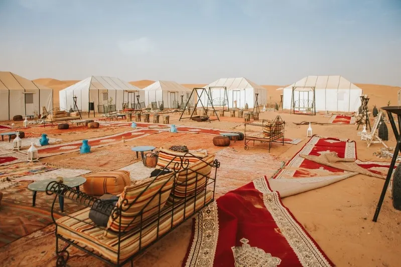 An expansive desert setting featuring numerous tents and pieces of furniture, blending nature with human habitation while day trip from marrakesh