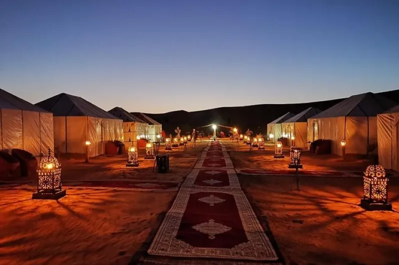 A serene desert trip in Morocco camp at night, featuring illuminated tents and soft lights, creating a tranquil atmosphere under the stars 