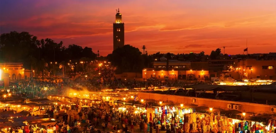 A panoramic view of Marrakech at dusk, showcasing vibrant colors in the sky and illuminated buildings against the horizon.While Marrakech Tours