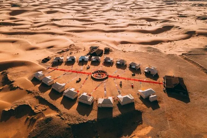 Aerial view of a desert camp featuring tents and a prominent red circle in the center of the scene.7 Days Tour from Fes