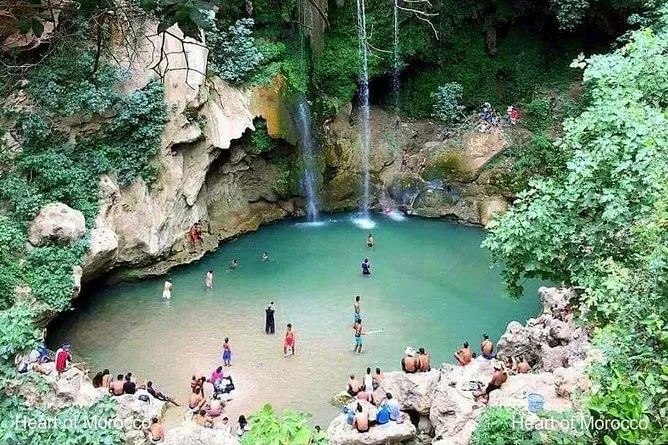 A group of people swims in a pool beside a cascading waterfall, enjoying a sunny day outdoors. Chefchaouen & Akchour Waterfalls Day Trip from Fes