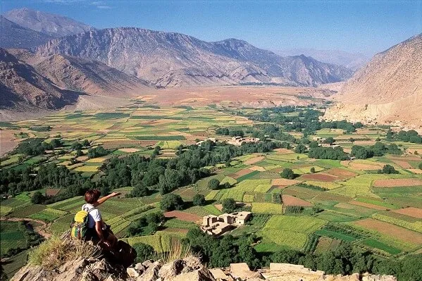A man sits on a rock, gazing out over a vast, scenic valley below him.