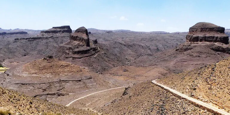 A winding road cuts through a mountainous desert landscape under a clear blue sky.