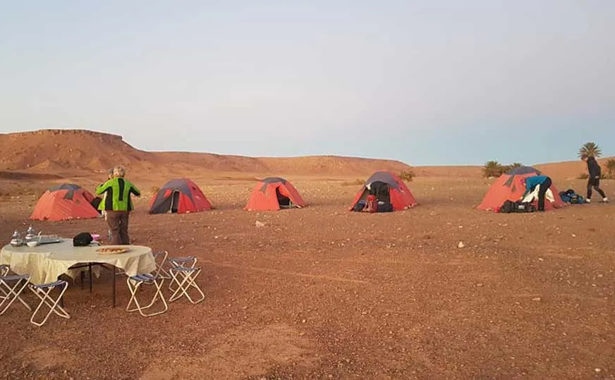 A group of tents in the desert with people sitting around them, enjoying the outdoors and socializing.