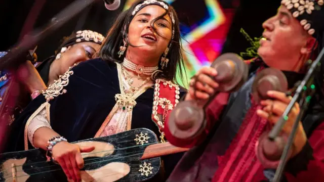 A woman in traditional attire plays a musical instrument, showcasing cultural heritage and artistry. Dinner Show with Gnaoua Music
