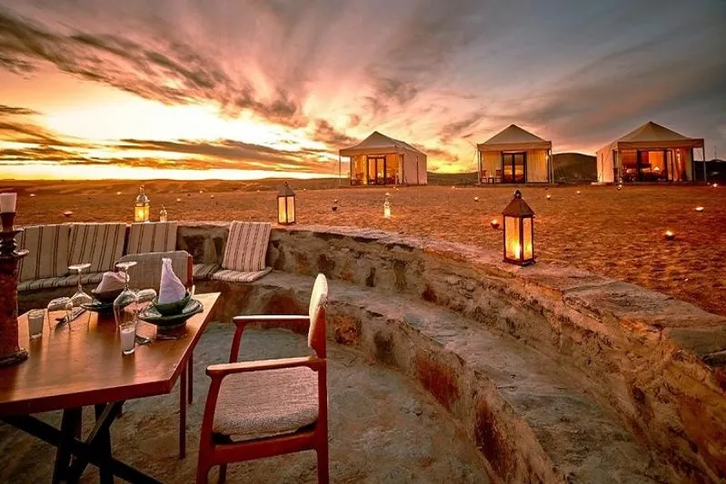 A table and chairs arranged on the beach, silhouetted against a vibrant sunset sky.7 Days Agadir to Imperial Cities & Desert Tour