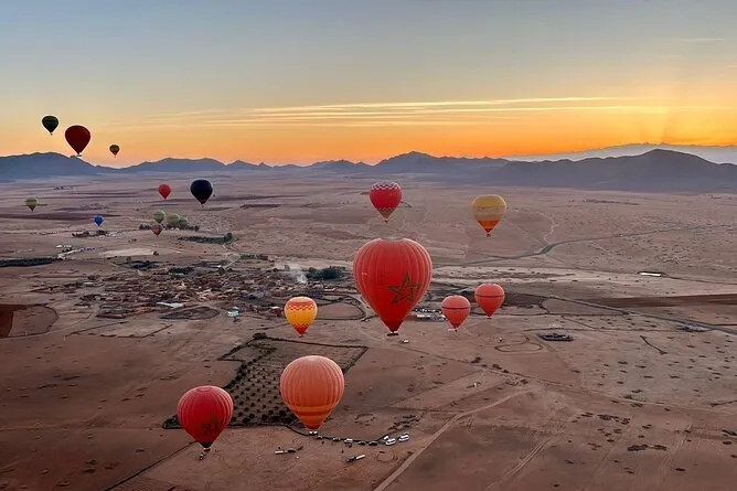 Hot air balloons float over a desert landscape during a vibrant sunset, casting colorful silhouettes against the sky.Vol en montgolfière au-dessus de Marrakech