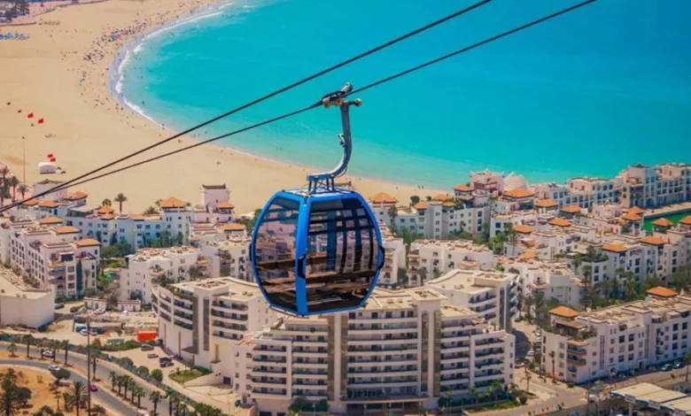 A cable car glides over a beach, offering a view of the ocean below.7 Days Agadir to Imperial Cities & Desert Tour