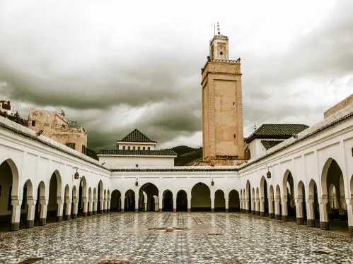 A serene courtyard of a Moroccan mosque, featuring intricate tile work and lush greenery under a clear blue sky.