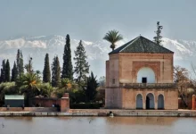 A building beside a pond with mountains rising in the background under a clear blue sky. Bird Watching at Menara Gardens