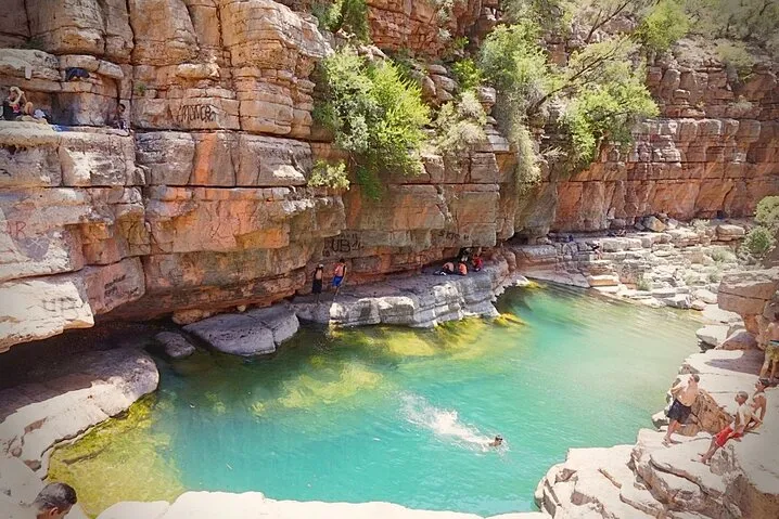 People swimming in a pool surrounded by natural rock formations under a clear blue sky.