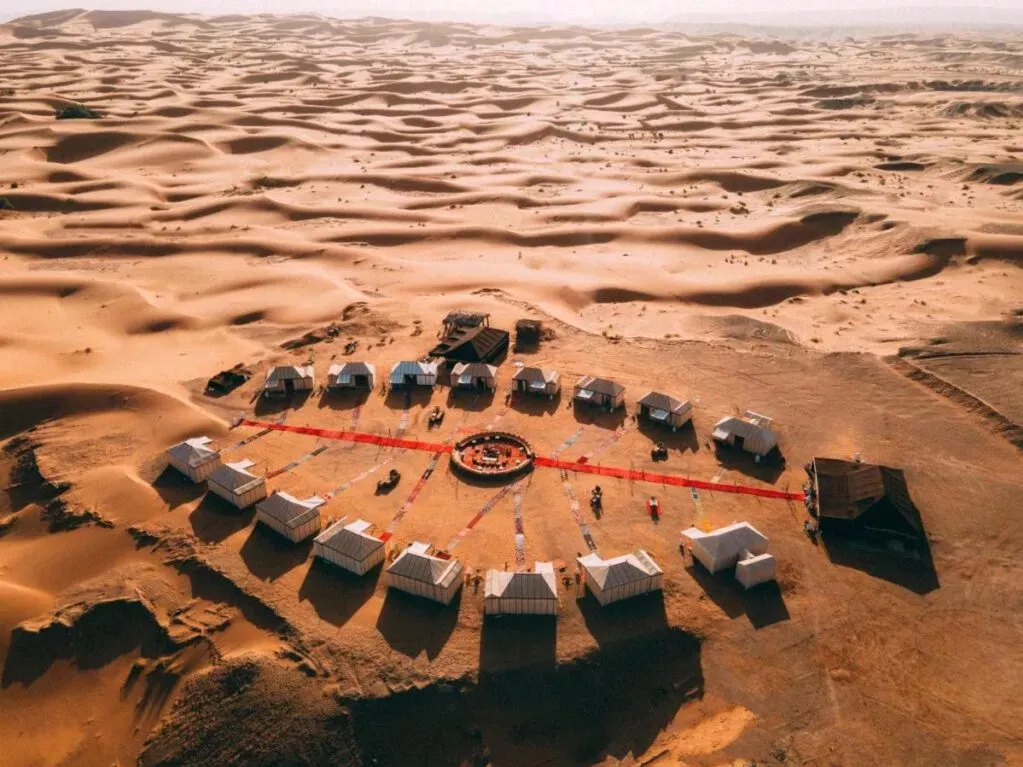 Aerial view of a desert camp featuring several tents arranged in a sandy landscape under a clear blue sky. 6 Days Marrakech to Sahara: Merzouga & Todra Gorges