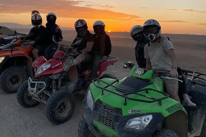 Four people riding ATVs in the desert during a vibrant sunset, with warm colors illuminating the landscape.