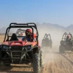 Four individuals riding all-terrain vehicles across a sandy desert landscape under a clear blue sky. Buggy Adventure in Agafay Desert