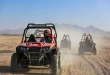 Four individuals riding all-terrain vehicles across a sandy desert landscape under a clear blue sky. Buggy Adventure in Agafay Desert