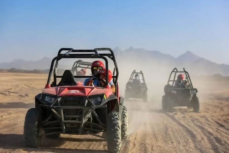 Four individuals riding all-terrain vehicles across a sandy desert landscape under a clear blue sky. Buggy Adventure in Agafay Desert