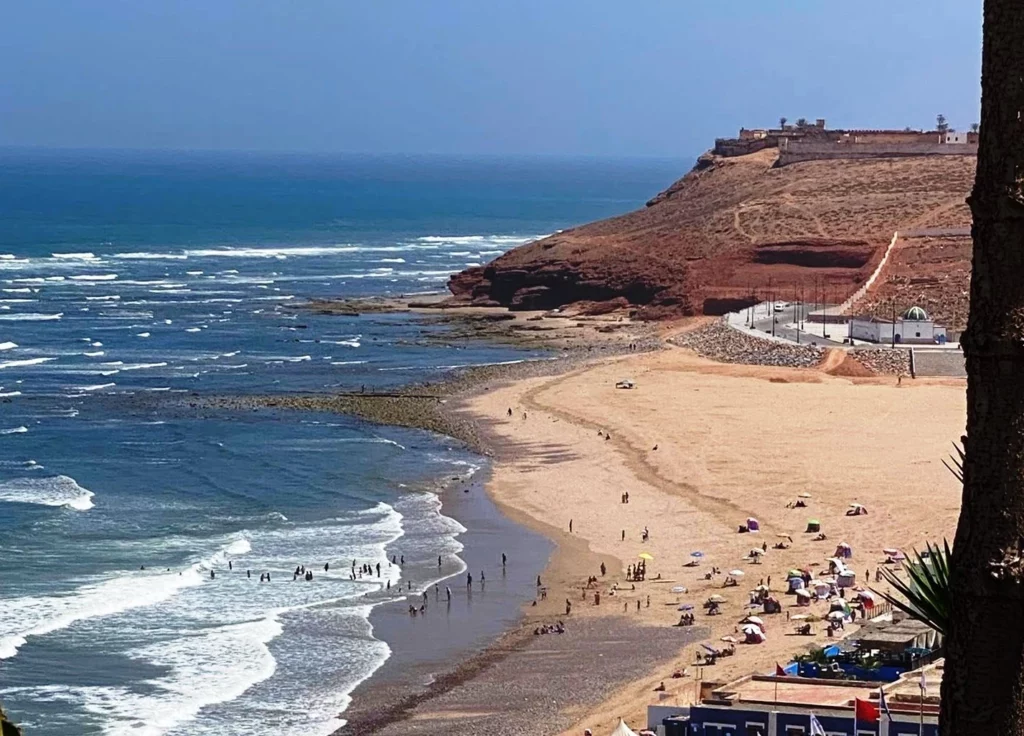 A beach scene with people enjoying the sun, framed by a towering cliff in the background.