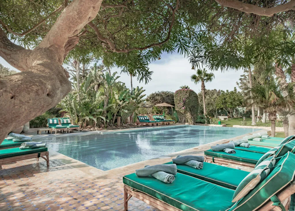 A pool surrounded by lounge chairs and green umbrellas, inviting relaxation under the sun.