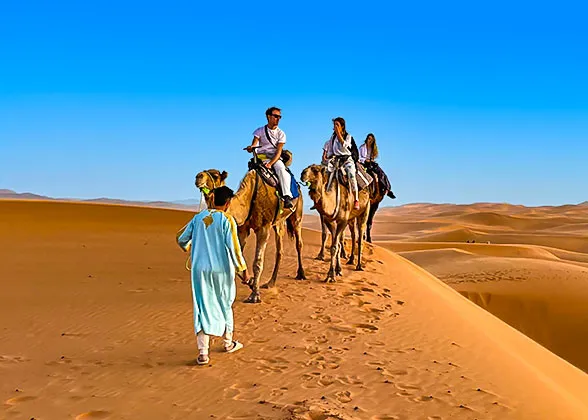 Three people riding camels across a vast desert landscape under a clear blue sky.