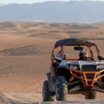 Two people riding an ATV through a vast desert landscape under a clear blue sky. Buggy Adventure in Agafay Desert