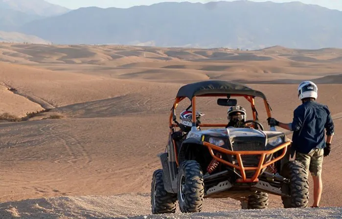 Two people riding an ATV through a vast desert landscape under a clear blue sky. Buggy Adventure in Agafay Desert