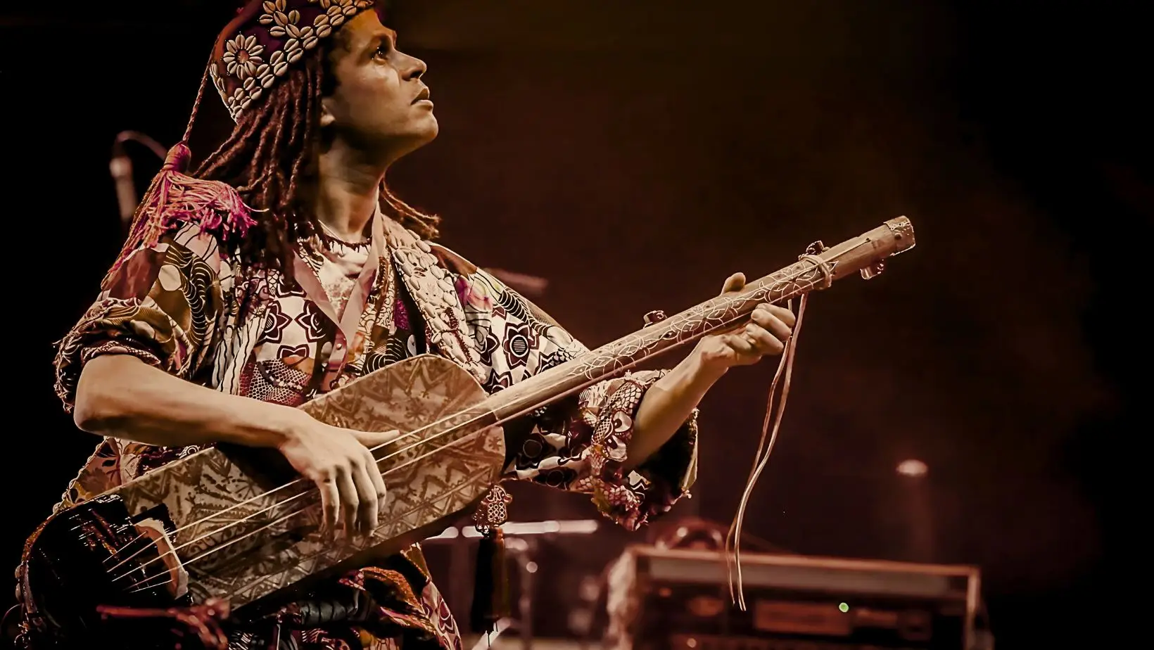 A man wearing a headdress plays an electric guitar, showcasing his musical talent and cultural expression.