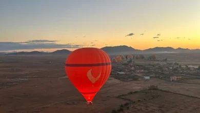 A red hot air balloon soaring above a vast desert landscape under a clear blue sky.Vol en montgolfière au-dessus de Marrakech