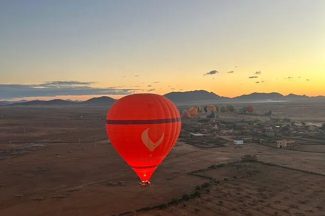 A red hot air balloon soaring above a vast desert landscape under a clear blue sky.Vol en montgolfière au-dessus de Marrakech