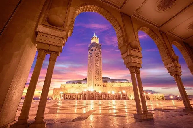 A mosque illuminated by warm sunset light, showcasing its architectural details against a colorful sky.12 Days Grand Morocco Tour