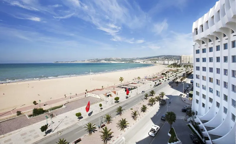 A beach scene featuring a hotel overlooking the ocean, with clear blue waters and a sunny sky in the background.12 Days Morocco Explorer Tour from Tangier