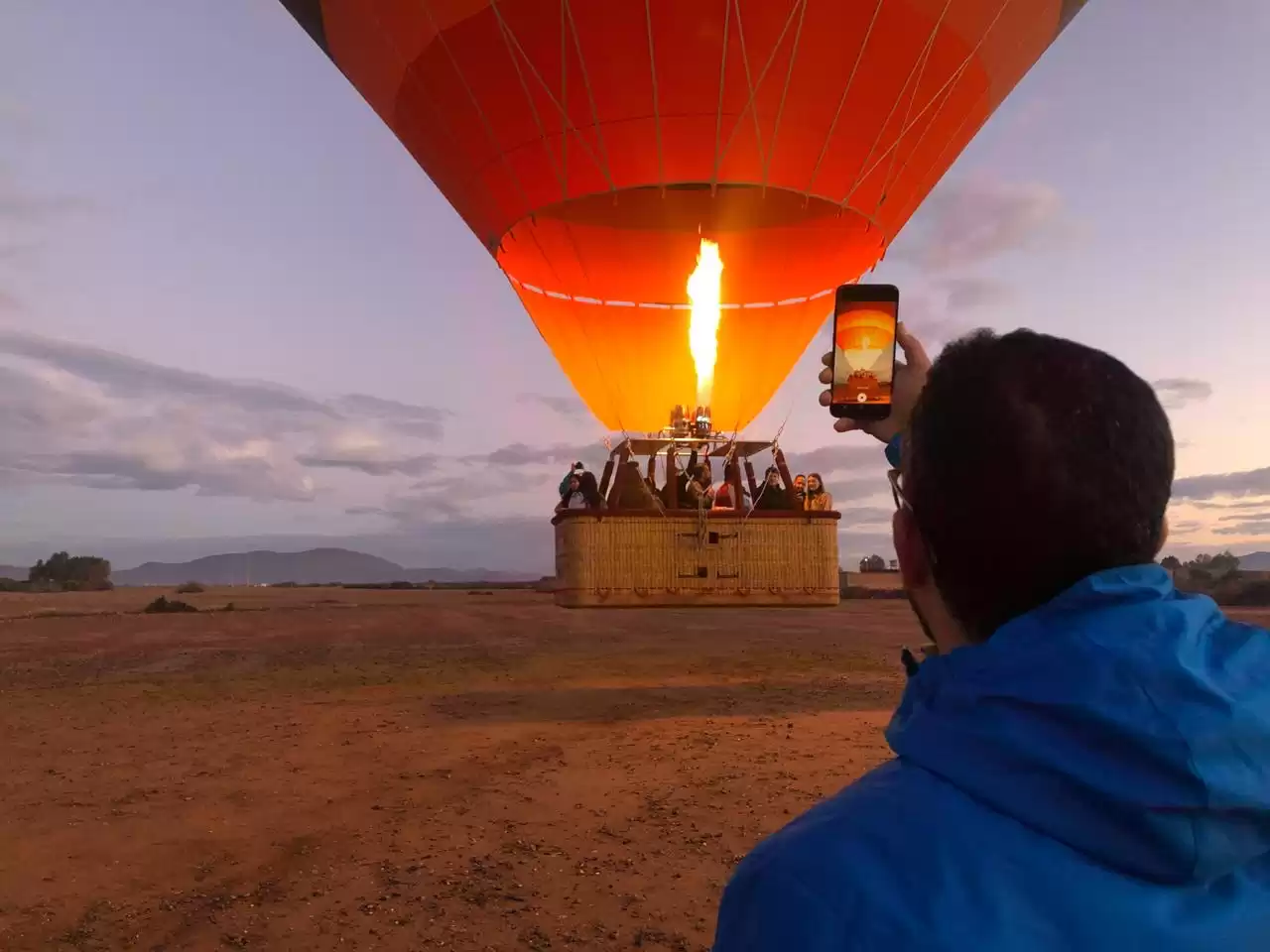 A man photographing a colorful hot air balloon against a clear blue sky.Vol en montgolfière au-dessus de Marrakech