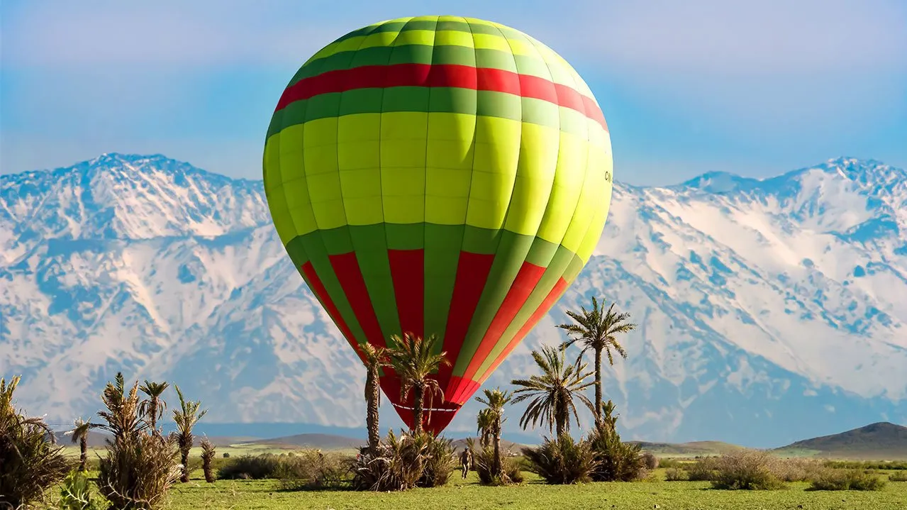 A colorful hot air balloon soars above majestic mountains under a clear blue sky. Balloon Ride over Marrakech