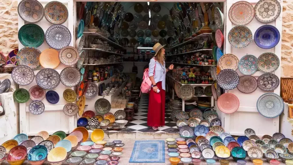 A woman stands in front of a shop displaying a variety of colorful plates in the window.