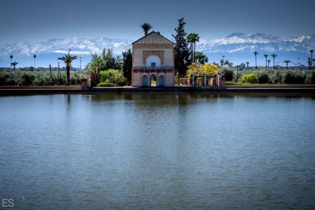 A small building is situated in the center of a tranquil lake, surrounded by calm water and distant trees. Bird Watching at Menara Gardens
