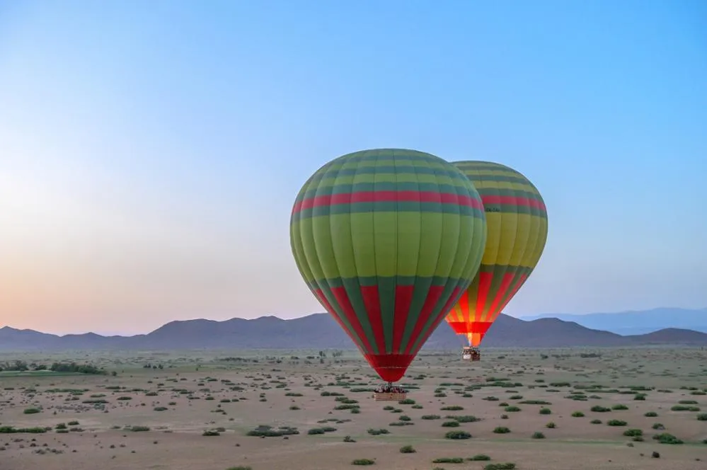 Hot air balloon soaring over a vast desert landscape under a clear blue sky.Vol en montgolfière au-dessus de Marrakech