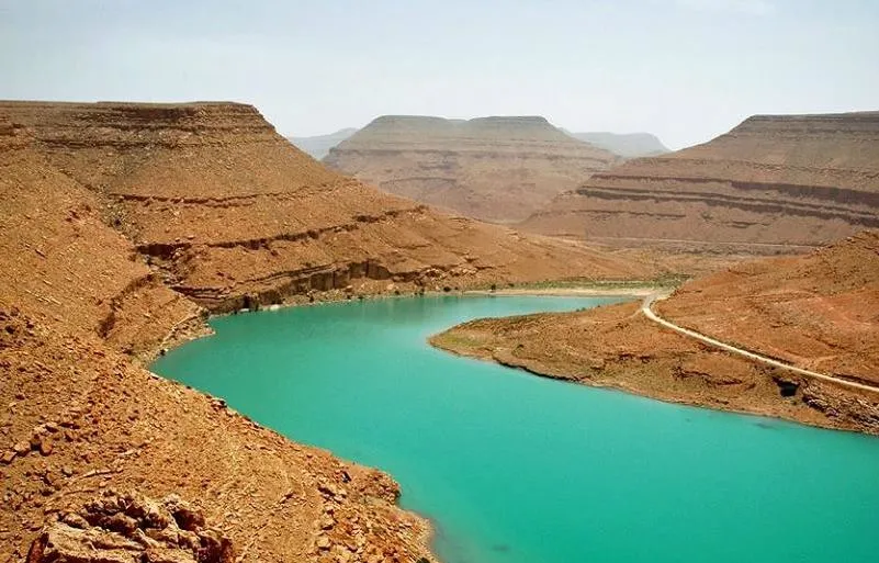 A serene blue lake nestled within a rugged canyon, surrounded by steep rock walls and lush vegetation. 5 Days Errachidia to Marrakech via Desert, Dades & Ouarzazate