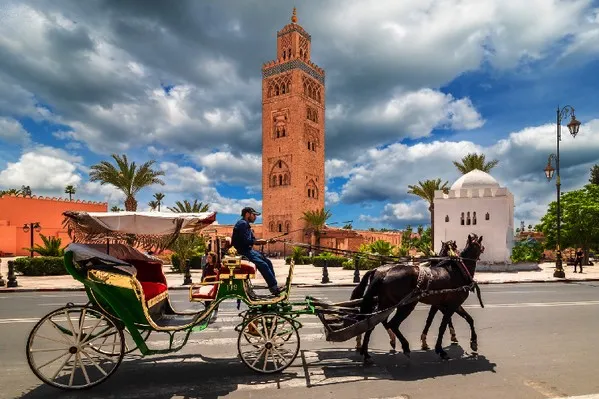 A horse and carriage are positioned in front of a historic clock tower, showcasing a charming urban scene. 5 Days Fes to Marrakech via Desert & Dades Valley