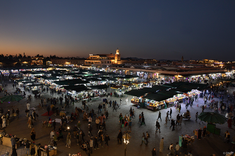 A large crowd of people shopping at a bustling night market, illuminated by colorful lights and vibrant stalls.