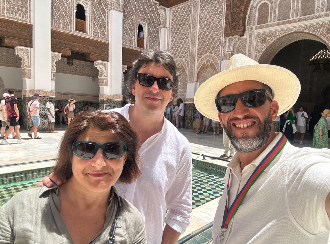 Licensed Moroccan guide explaining the history of the Madrasa Ibn Yusuf to a visitor