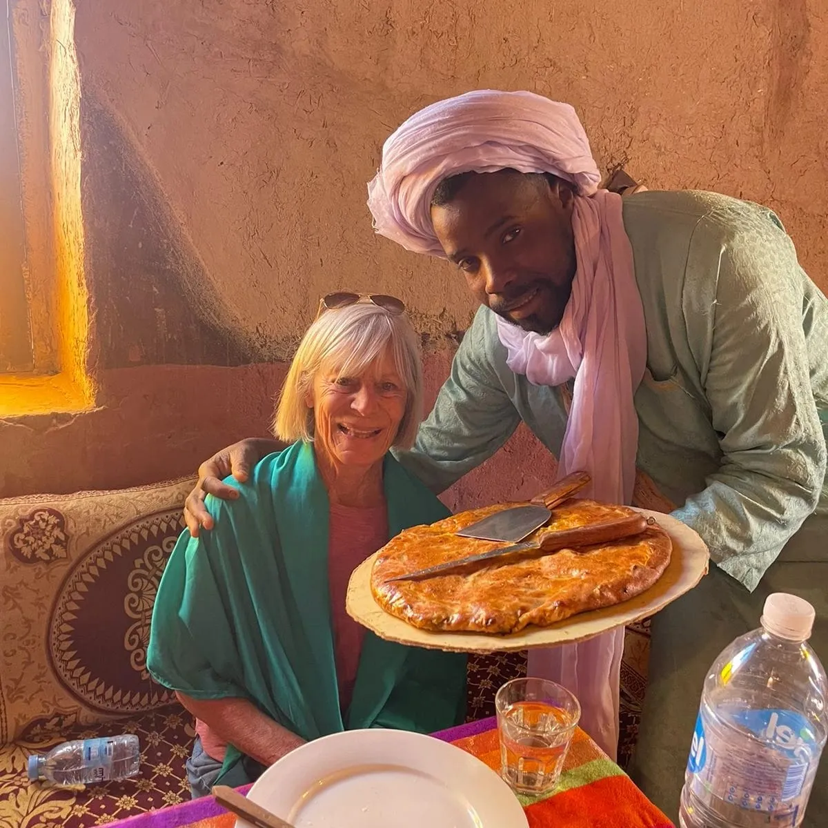 Guide presenting fresh Madfouna Berber Pizza to tourists in Morocco desert