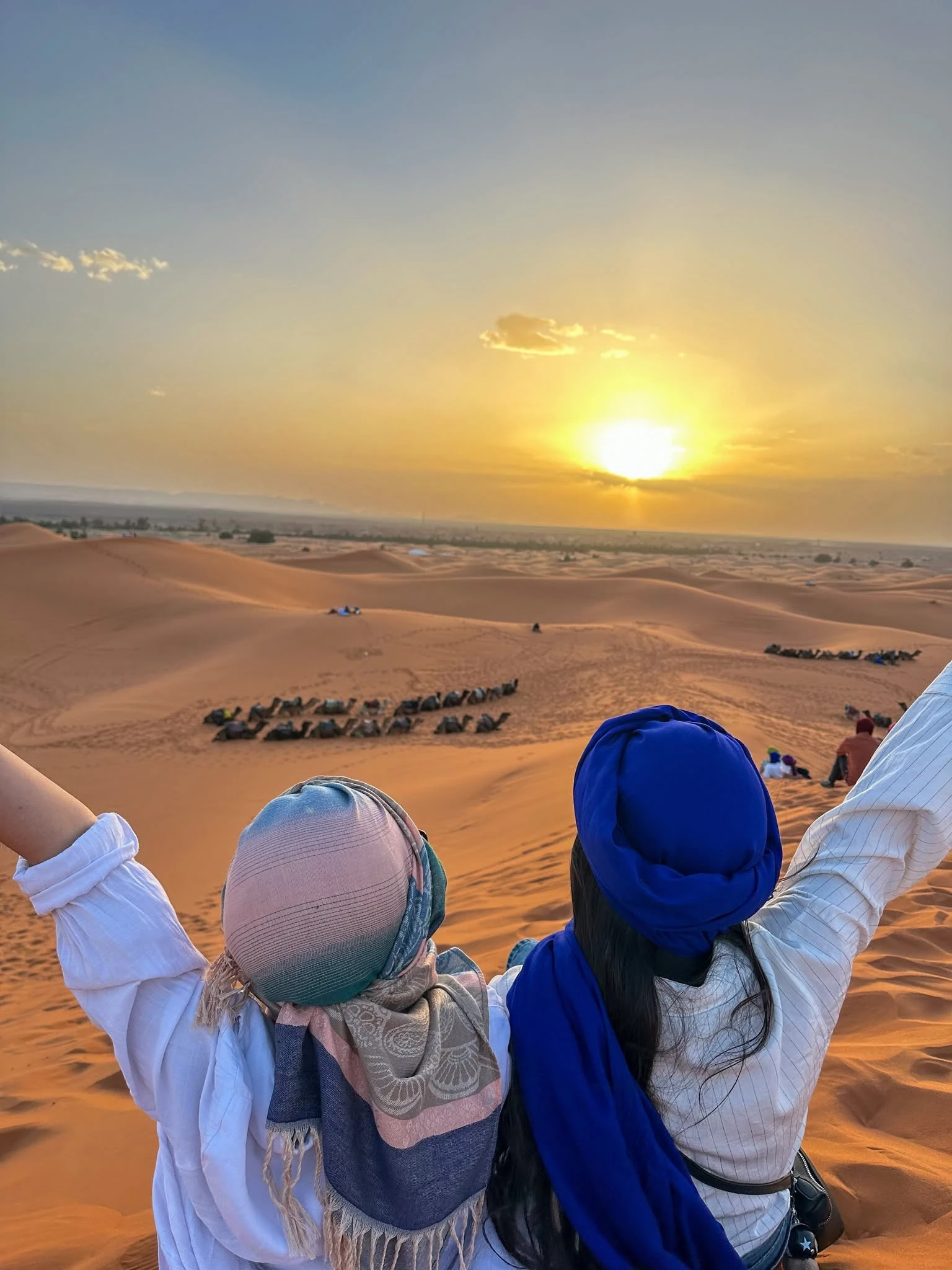 Deux silhouettes marchant sur une crête de dune près d'un campement désertique au crépuscule près de Merzouga