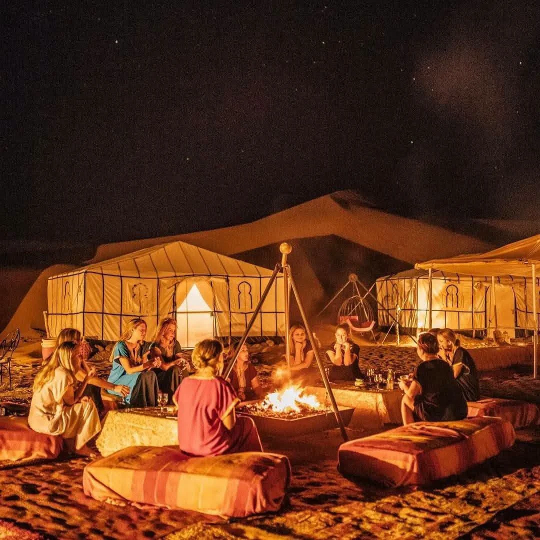 Two figures walking along a dune ridge near a desert camp at dusk outside Merzouga